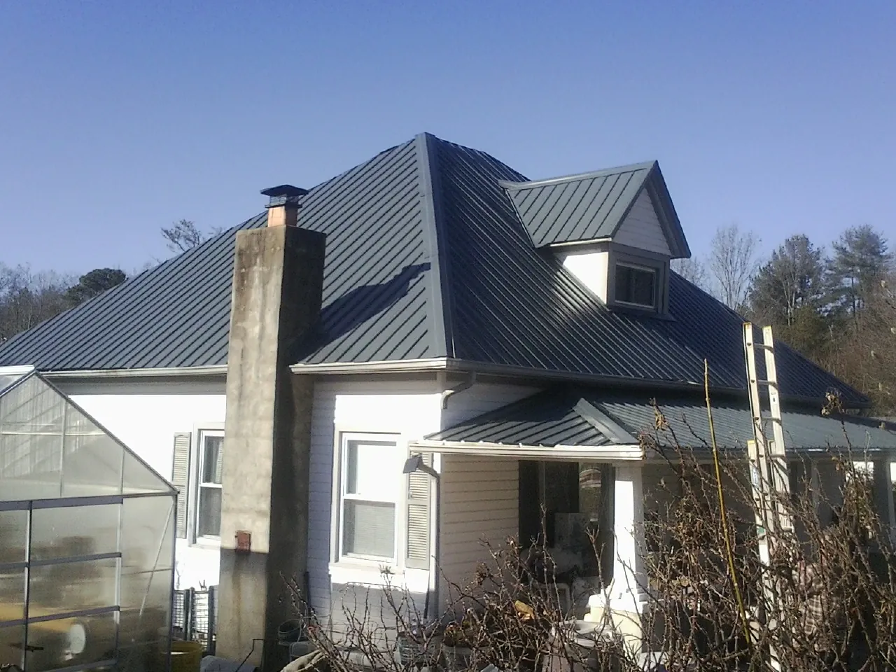 Dark blue standing seam metal roof on a white farmhouse with dormer — Slate & Tile Roof Repair by Roofing Brothers in Cade