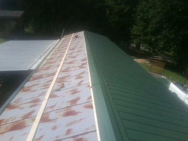 Old rusted panels beside newly installed green metal roofing — Wind Damage Roof Repair by Roofing Brothers in Cade