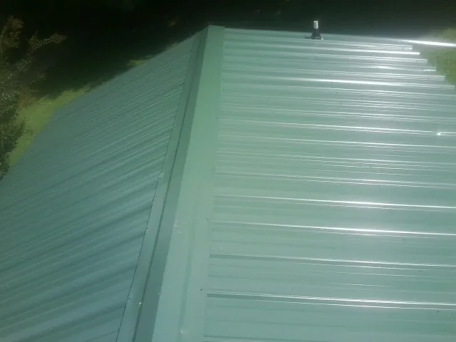 New green metal panels meeting at the ridge of a roof — Flat Roof Repair work by our crew in Cade