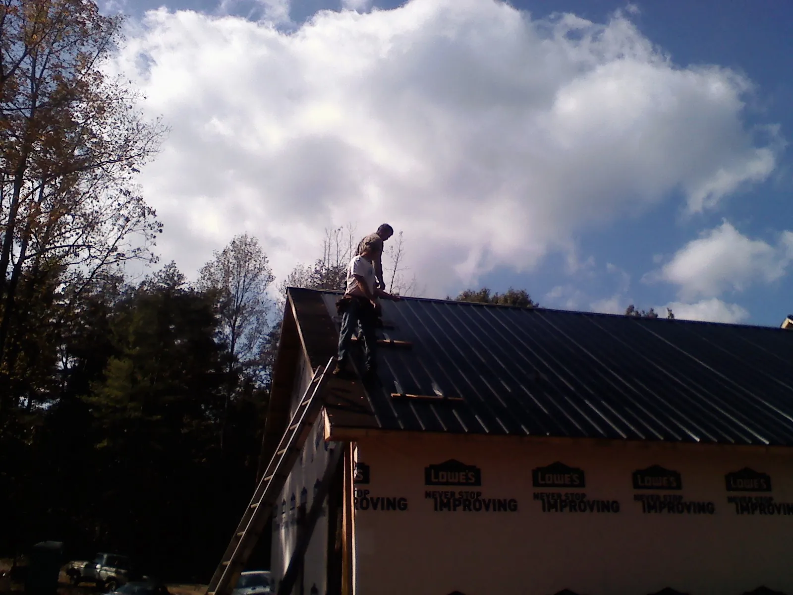 Roofer fastening dark metal panels high against a cloudy sky, from a Roof Inspection job in Cade
