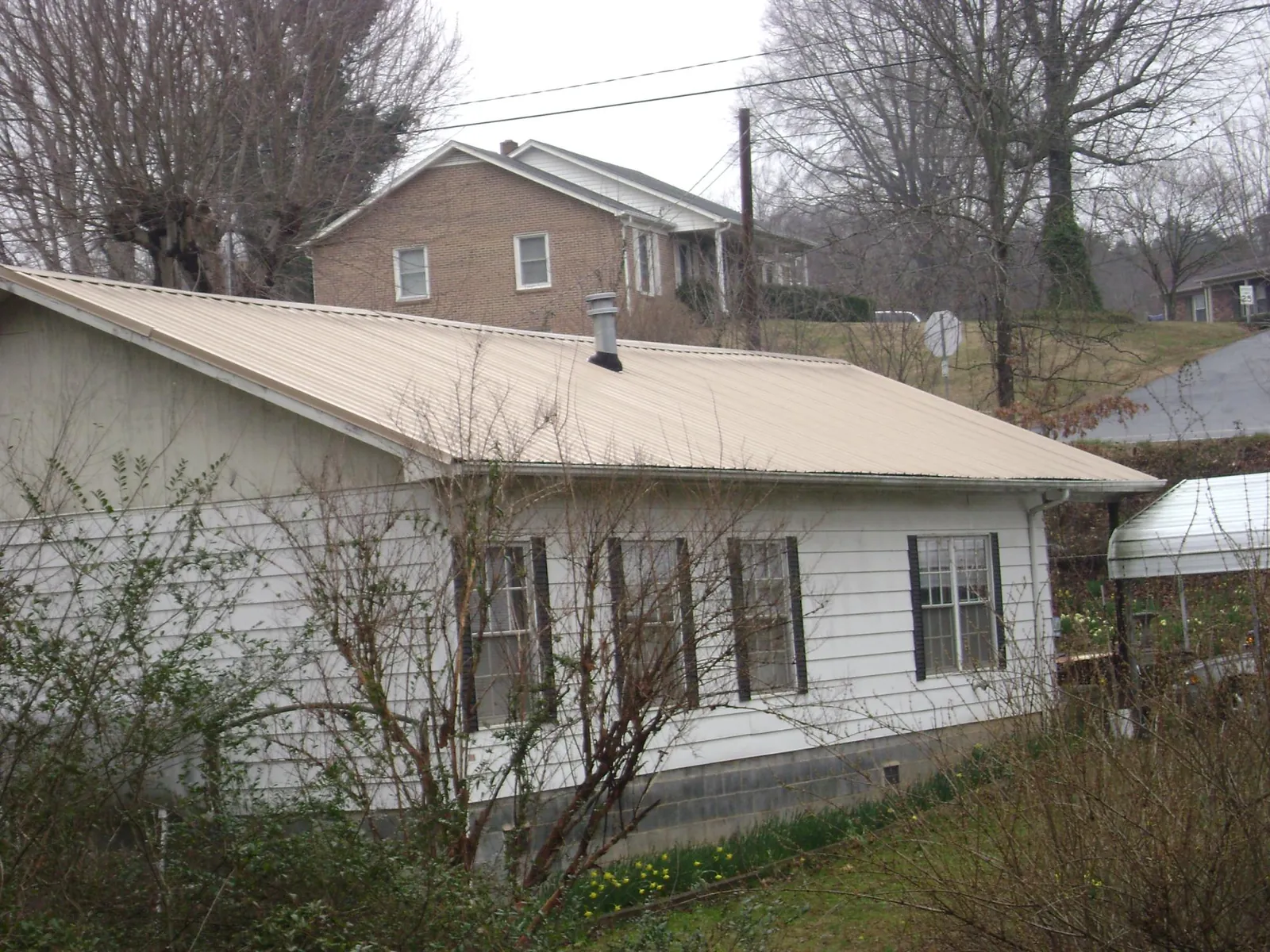 Tan metal roof on a white sided house set into a hillside — Commercial Roofing by Roofing Brothers in Cade